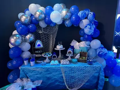 Birthday party table setup with blue, white, and silver balloons, desserts, and nautical decorations.